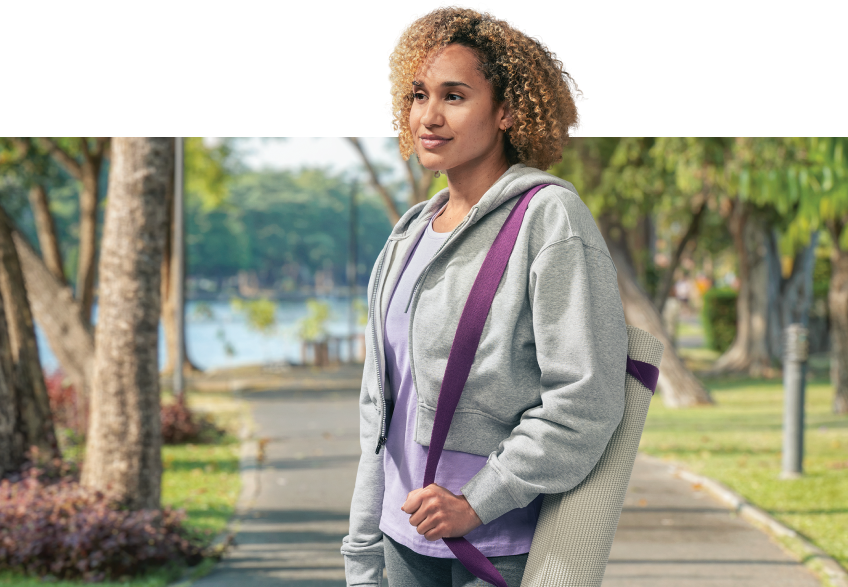 Patient standing in a park with a yoga mat rolled up and hanging on shoulder
