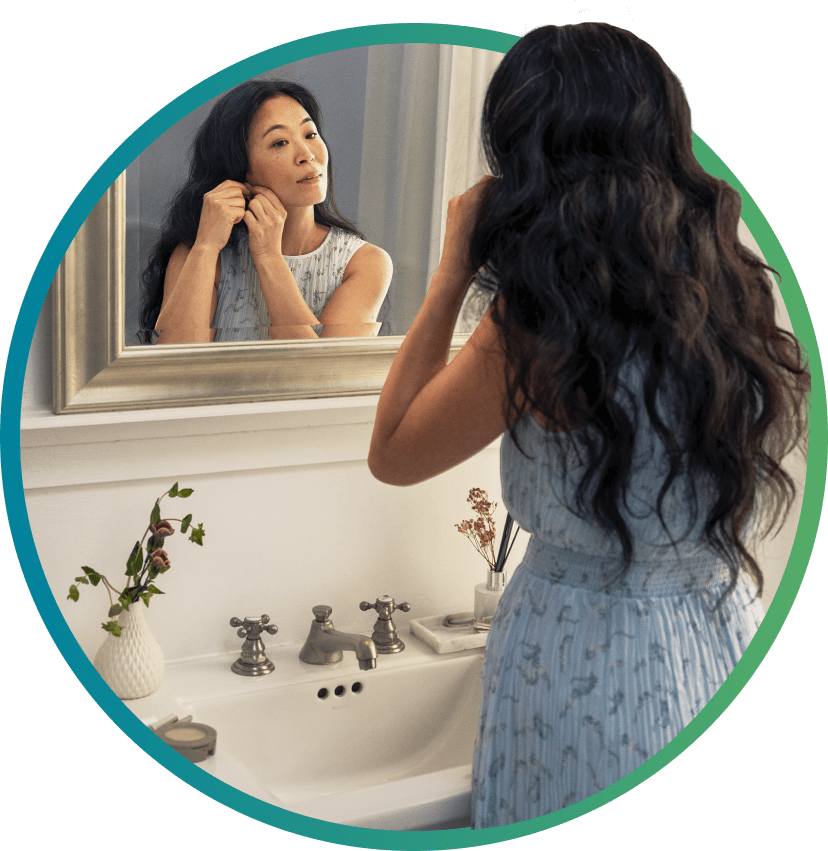 woman putting on earrings in bathroom mirror